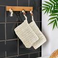 Two beige soap saver bags hanging on a wooden rack against a black tiled wall with a plant in the corner.