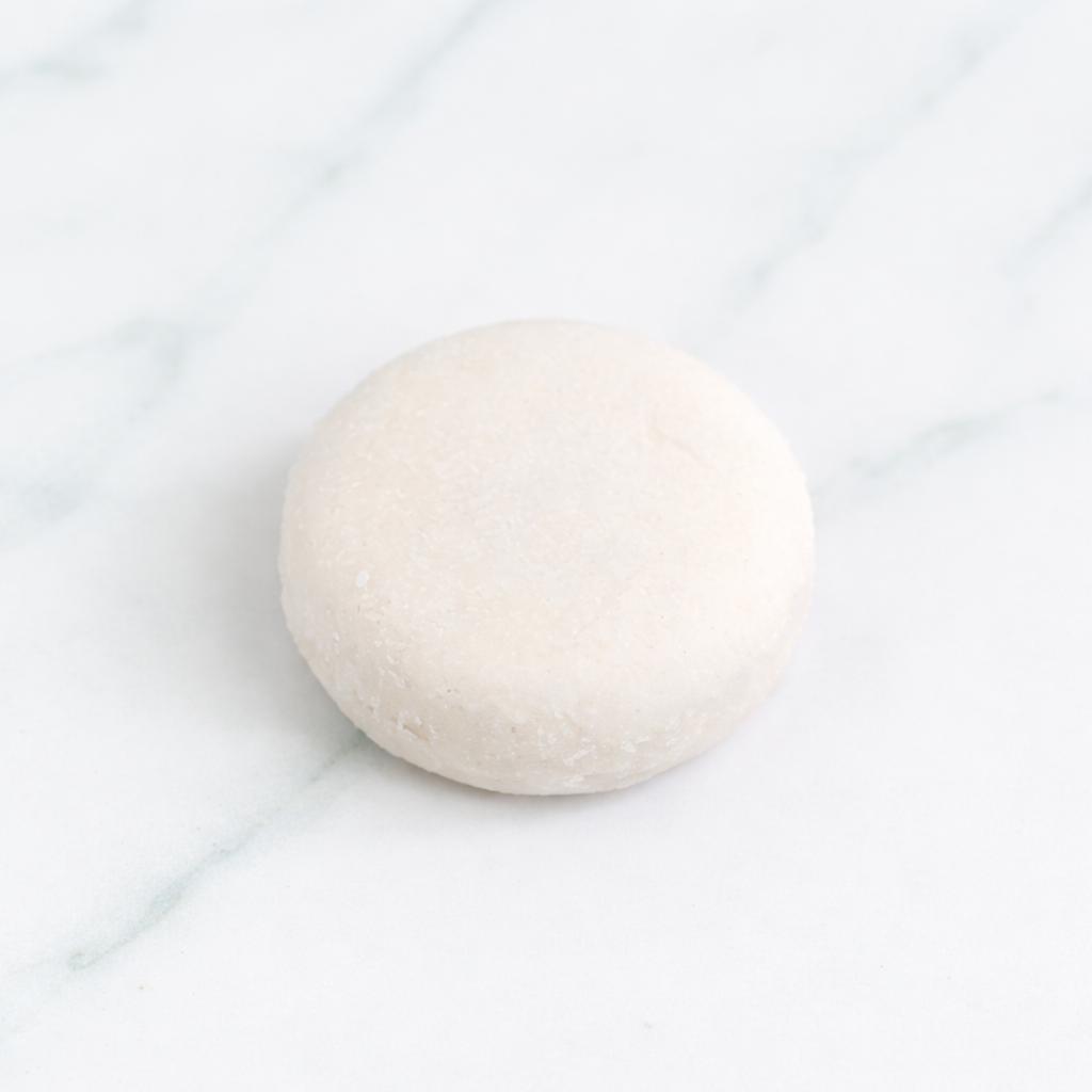 A professional product image of a textured white Citrus Mint Shampoo Bar on a marble surface. Fresh mint sprigs and citrus fruit slices are artfully placed around the bar to highlight its invigorating and deep-cleansing natural ingredients.