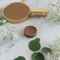 A circular, brown hair conditioner bar displayed on a clean white background with leaves and flowers.